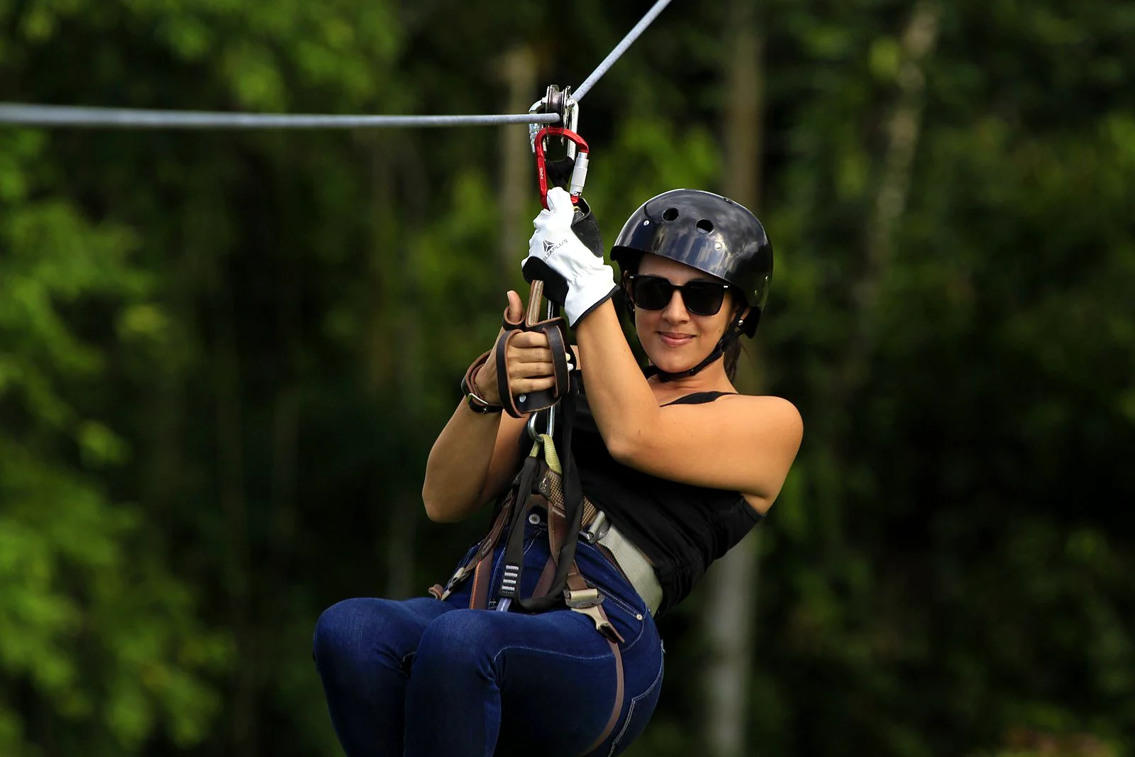 Smiling woman hanging from a zipline trolley above the Arenal rainforest canopy