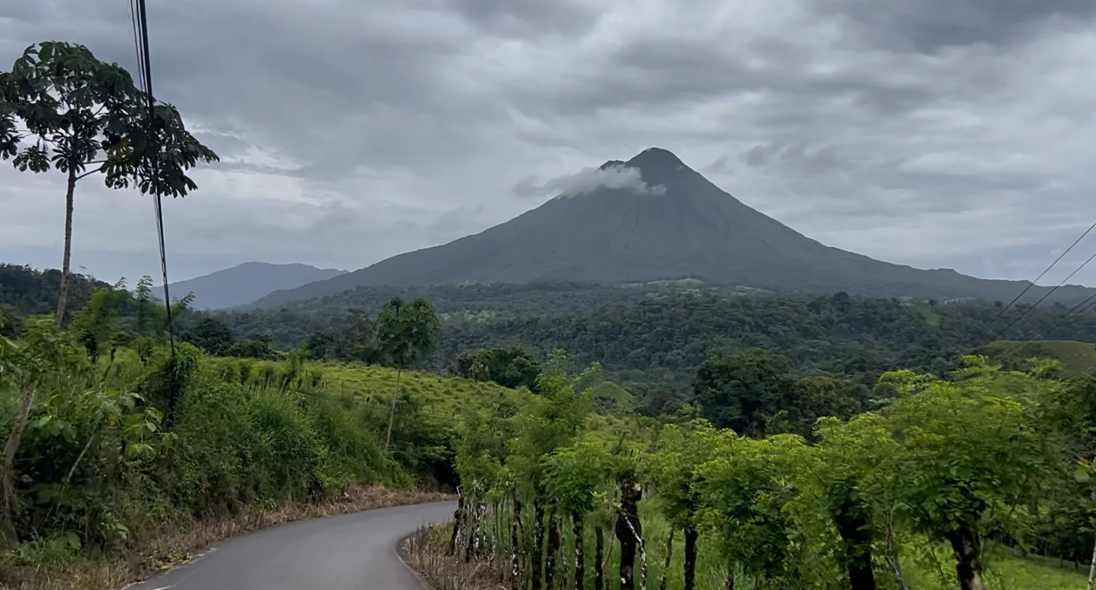 Country road curving past green pasture toward Arenal Volcano near La Fortuna