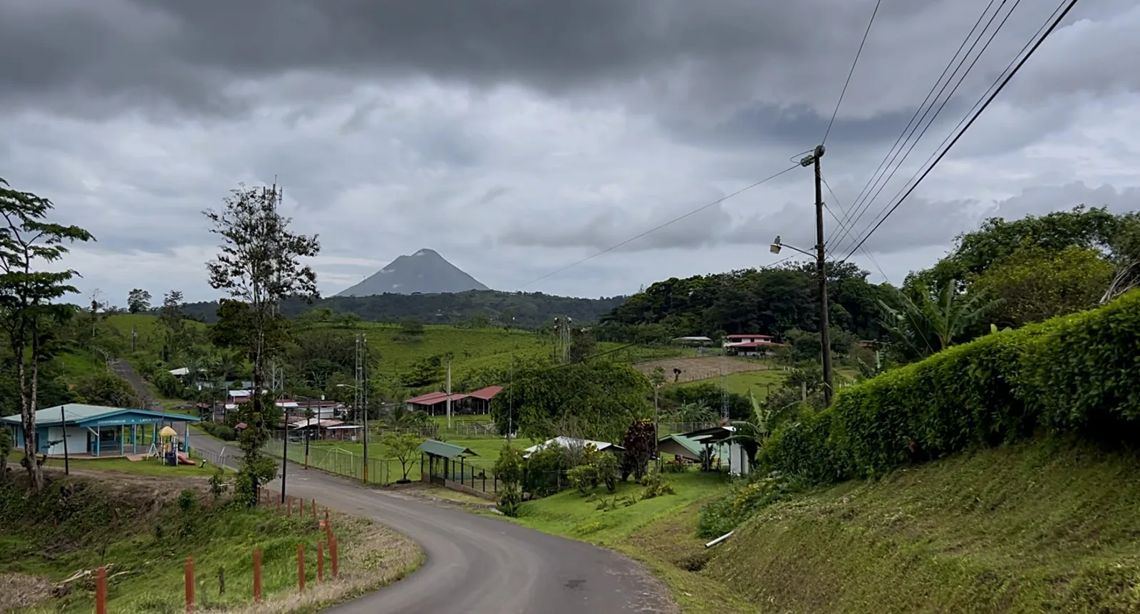 Paved road curving down into a small village near La Fortuna, with Arenal Volcano on the horizon